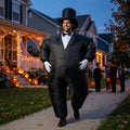 Adult in inflatable tuxedo costume with top hat and white gloves on a Halloween porch path