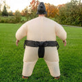 Back view of inflatable sumo wrestler costume with beige body, black belt and black topknot on grass